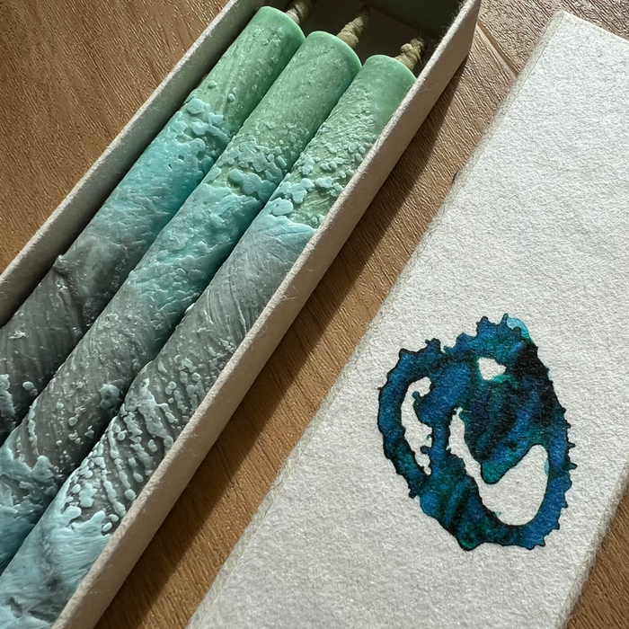 Set of textured candles in a box with a decorative logo on a wooden surface