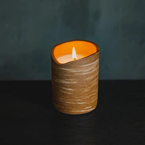 Candle in a textured brown container with a dark background