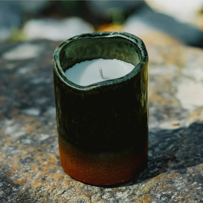 Candle in a green ceramic holder on a rocky surface