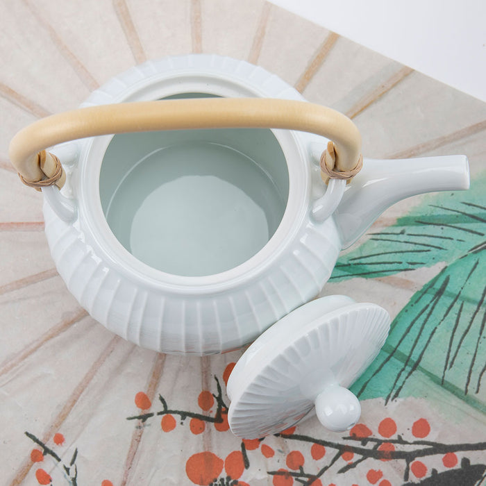 White ceramic teapot with a beige handle on a decorative surface with floral patterns.
