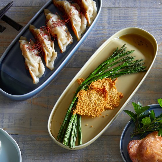 Food platter with gyoza, asparagus, and chicken on a wooden surface.