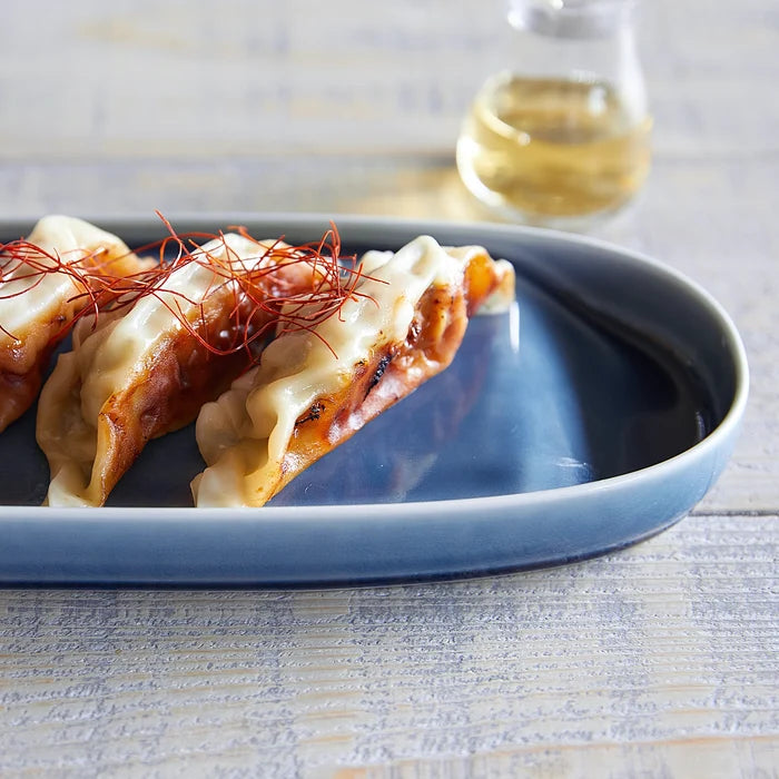 Three gyozas on a blue plate with a glass of white wine in the background.
