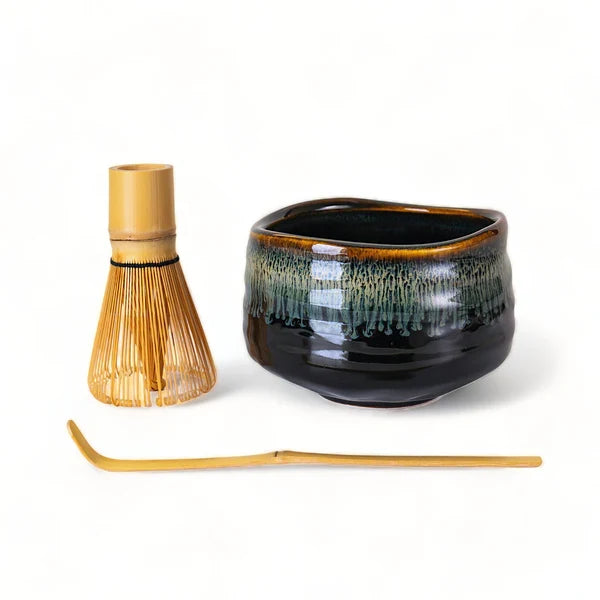 Ceramic bowl with bamboo whisk and spoon on a white background.