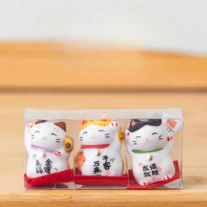 Three small ceramic cat figurines in packaging on a wooden surface