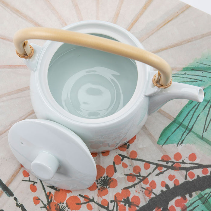 White ceramic teapot with a wooden handle on a decorative surface with floral patterns.