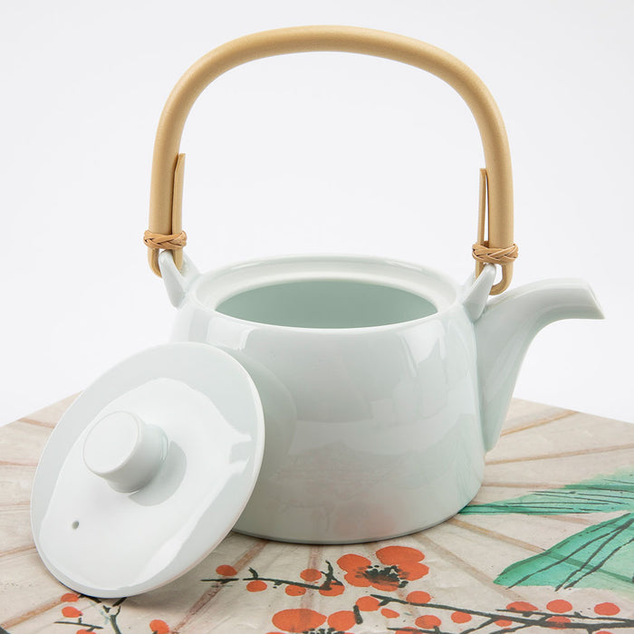 White ceramic teapot with a bamboo handle on a floral-patterned surface