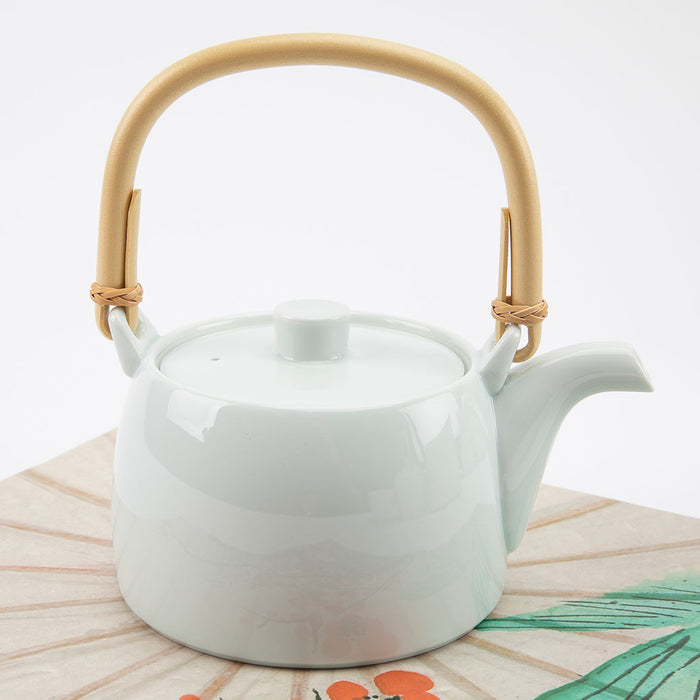 White ceramic teapot with a bamboo handle on a light wooden surface.