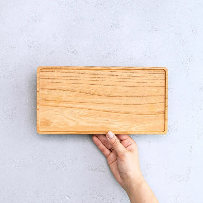 Wooden cutting board held by a hand on a light gray background