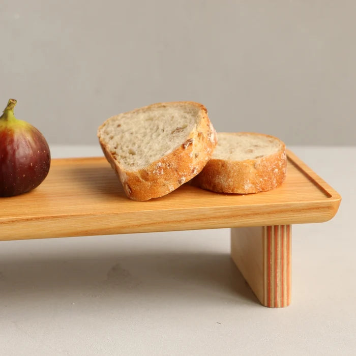 Two slices of bread on a wooden stand with a fig beside it on a neutral background