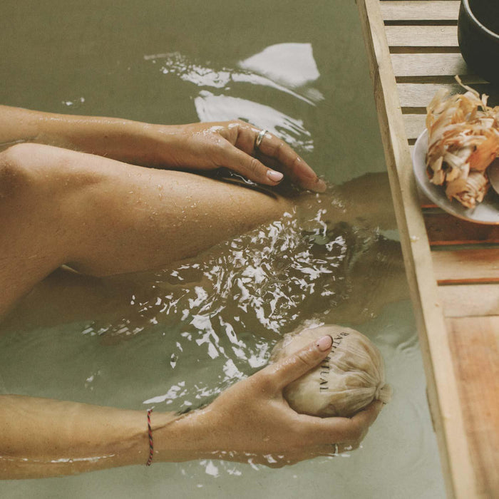 Person relaxing in a hot tub with a coconut, surrounded by wooden elements.