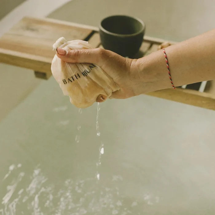 Hand holding a bath pouf over a bathtub with water flowing.